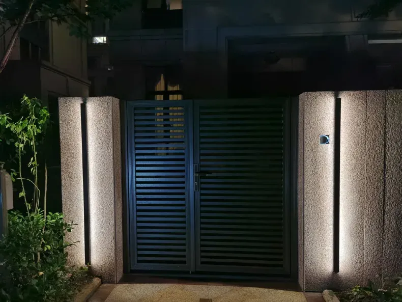 מנורת קיר LED אנכית מוארת ליד שער חצר בלילה