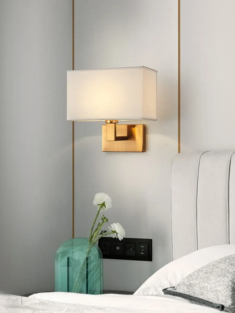 מנורת קיר מרובעת עם בסיס זהב ליד מיטה לבנה