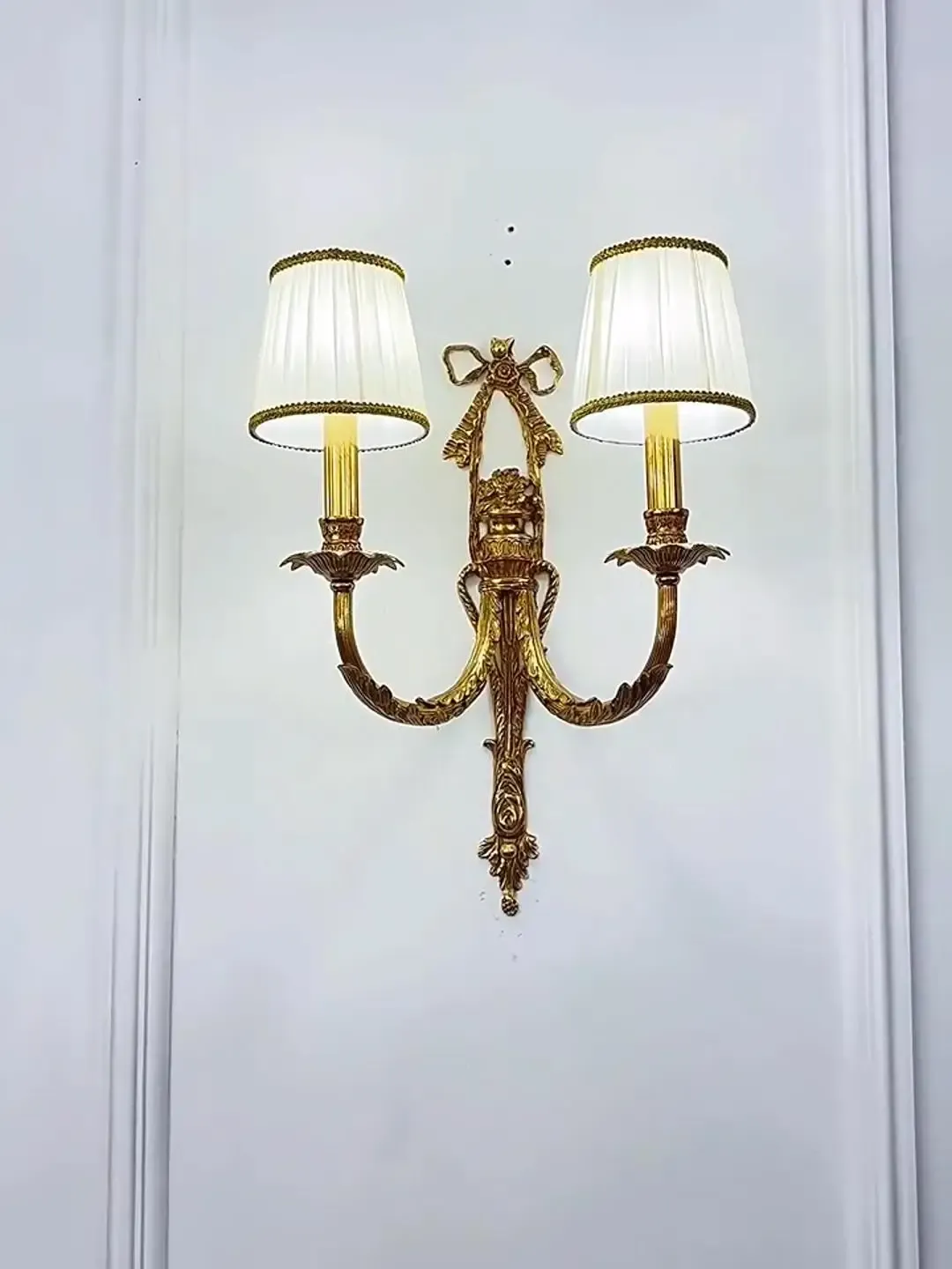 מנורת קיר ברונזה כפולה עם אהילים לבנים על קיר לבן