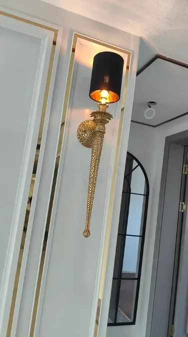 מנורת קיר נחושת עם אהיל שחור ליד דלת אפורה